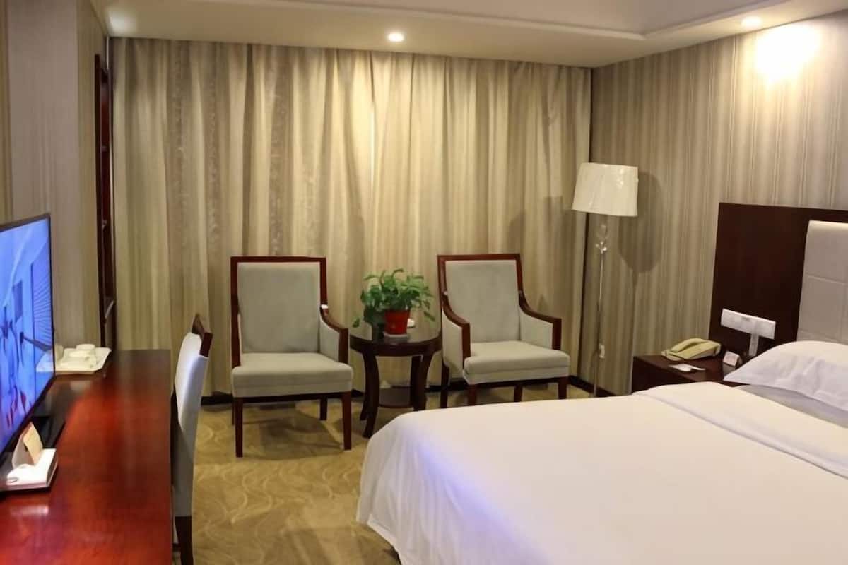 Een hotelkamer met een bed, twee fauteuils, een bureau met een televisie, een lamp en een nachtkastje.