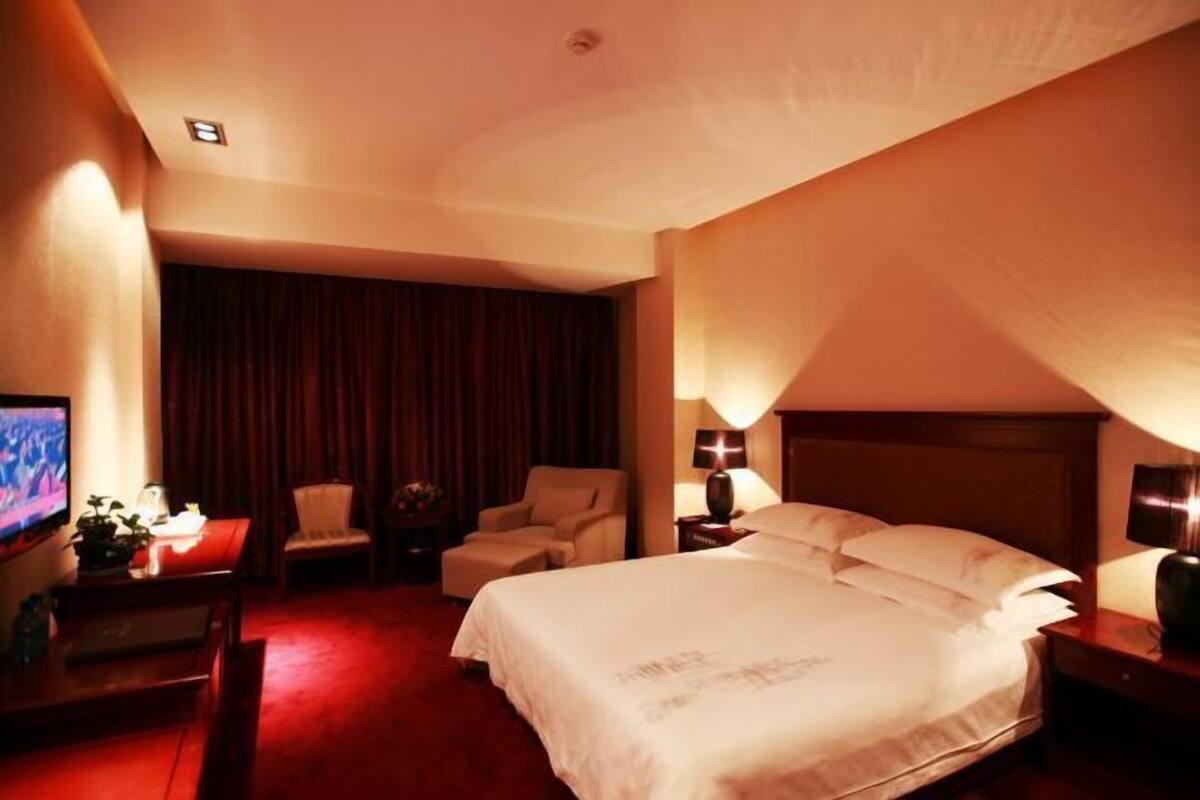 Een hotelkamer met een bed, een bureau met een computer, een stoel, een televisie en een gordijn.