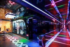 A brightly lit corridor with neon lights, a store on the left, and a seating area with a table and chairs. - Yinhe Hotel (Hancheng)