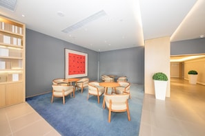 A modern interior with a blue carpet, a round table with chairs, a bookshelf, and a framed artwork on the wall. - Ji Hotel (Beijing)