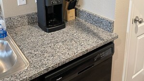 Une cuisine équipée d’un appareil à café intégré, d’un égouttoir à vaisselle et d’un meuble contenant de la verrerie et des bols.