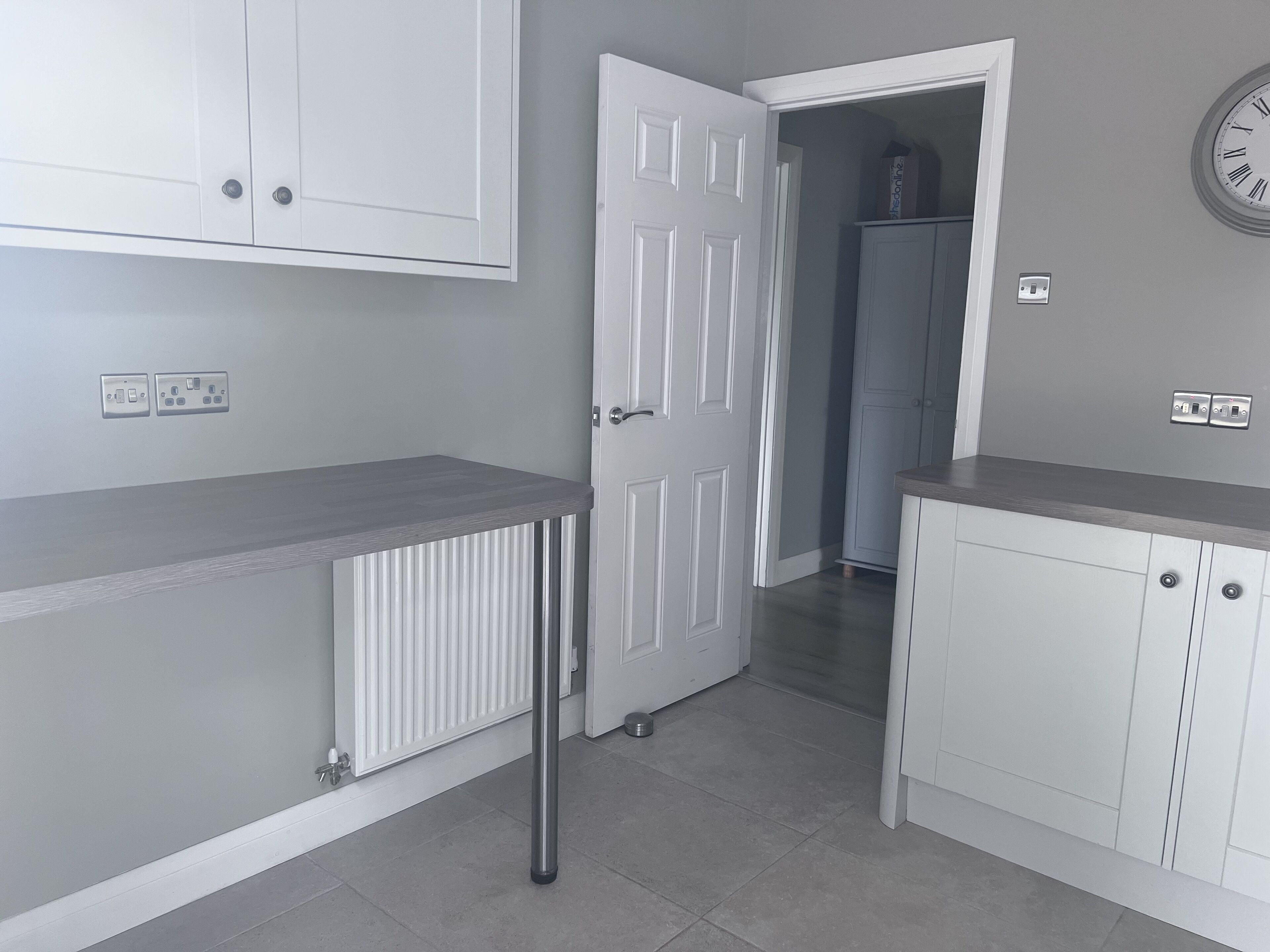 A kitchen with white cabinets, a grey countertop, and a white door leading to another room.