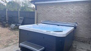 Un bain à remous avec des marches et un couvercle, situé à l’extérieur, à côté d’un mur en briques et d’une clôture en bois.