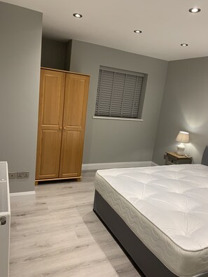 Ein Schlafzimmer mit Bett, Schrank, Fenster mit Jalousien und einer Nachttischlampe.