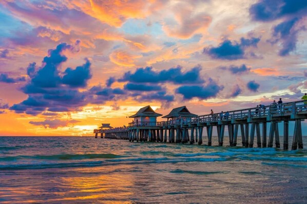 A pier extending into the sea with overwater bungalows and a sunset in the background.