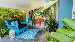 A covered patio with a blue patterned rug, a turquoise wicker sofa, and a red and blue table with chairs. - Lush, Secluded Pool + 5 Mins to Beach (Naples)