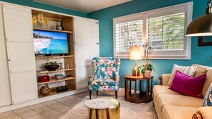 A living room with a TV, floral armchair, round coffee table, and a beige sofa with a purple pillow. - Lush, Secluded Pool + 5 Mins to Beach (Naples)