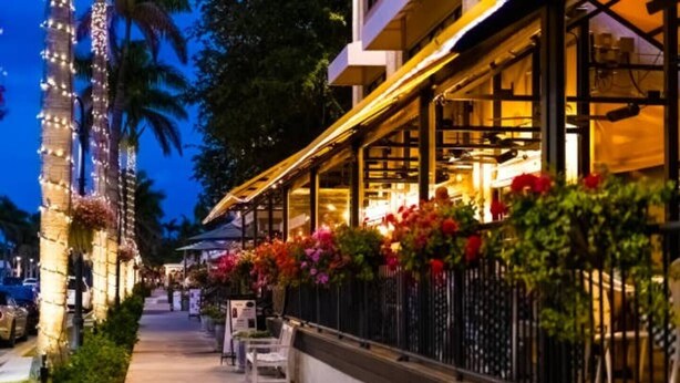 A restaurant with outdoor seating, a railing with flowers, and palm trees. - Lush, Secluded Pool + 5 Mins to Beach (Naples)