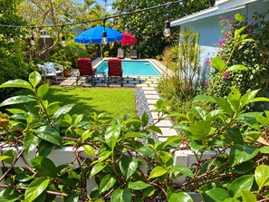 A backyard with a swimming pool, red and blue umbrellas, and outdoor seating.