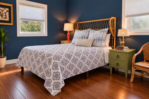 A bedroom with a bed, two nightstands, a chair, a potted plant, and a window with blinds.
