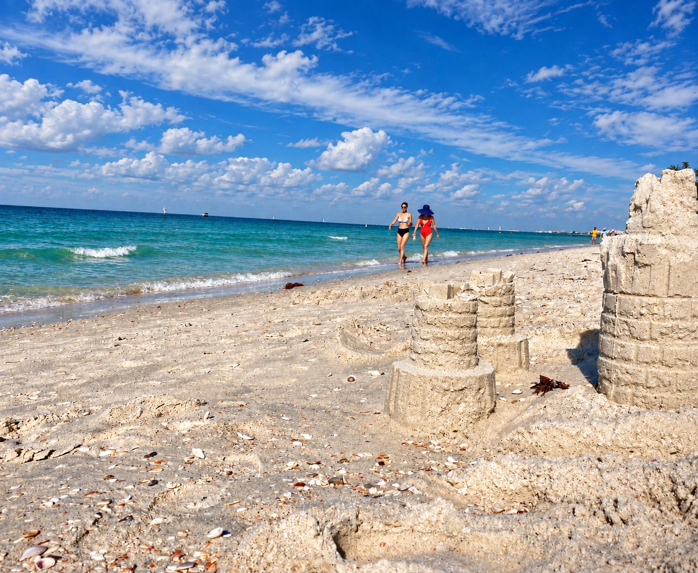 A beach with clear skies, two people walking, and ancient stone ruins.