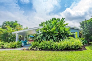 A modern house with a covered patio, lush greenery, and a clear sky.