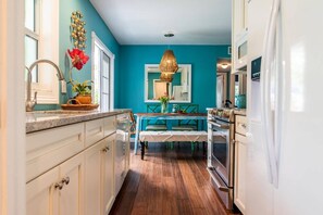 A narrow kitchen with teal walls, white cabinets, and a wooden floor.