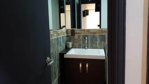 Une salle de bain avec un lavabo blanc, des meubles sombres et un mur recouvert de carreaux.