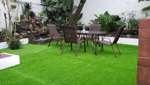 Une terrasse avec une table et des chaises en verre, entourée d’une végétation luxuriante et d’un petit jardin de rocaille.