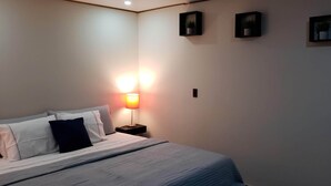Un lit bien fait, avec une literie blanche et grise, un oreiller noir et une lampe de chevet.