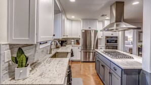 Una cucina moderna con mobili bianchi, elettrodomestici in acciaio inossidabile e un piano di lavoro in marmo.