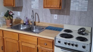A kitchen with wooden cabinets, a stainless steel sink, a gas stove, and a tiled backsplash. - Stardust Motel (Duncannon)