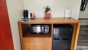 A compact kitchenette with a microwave, a black refrigerator, a coffee maker, a red plant, and a white speaker. - Stardust Motel (Duncannon)
