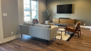 A modern living room with a grey sofa, wooden cabinet, and a flat-screen TV mounted on the wall. - North Lincoln, Minutes from Pinnacle Bank Arena and Memorial Stadium (Lincoln)