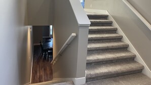 A staircase with carpeted steps and a white handrail, leading to a room with a wooden floor and a dining area visible in the background. - North Lincoln, Minutes from Pinnacle Bank Arena and Memorial Stadium (Lincoln)