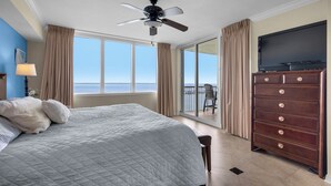 Une chambre d’hôtel avec un lit, une commode, une télévision et un balcon donnant sur l’océan.