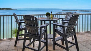Un balcon avec quatre fauteuils Adirondack, une table ronde et une bouteille de vin. Le balcon donne sur une étendue d’eau, avec une jetée visible au loin.