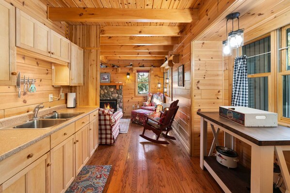 A wooden cabin interior with a kitchen, dining area, and a fireplace. - Northern Exposure Oscoda Cottage (Oscoda)