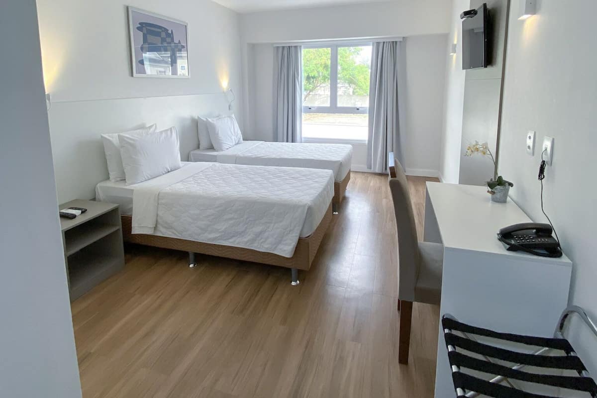 Een moderne hotelkamer met twee bedden, een bureau, een stoel, een televisie en een raam met gordijnen.