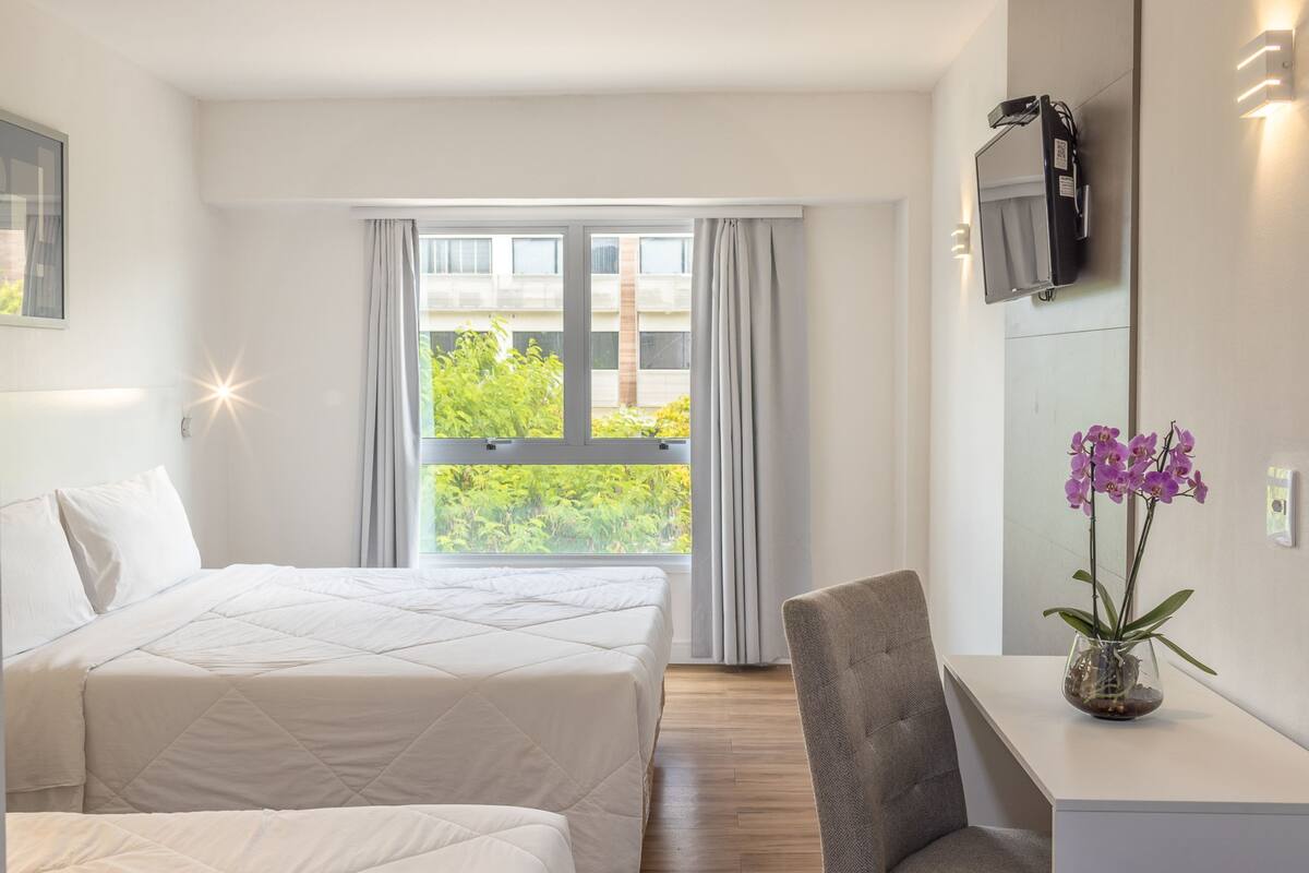 Een hotelkamer met een bed, bureau, stoel, een aan de muur bevestigde televisie en een raam met gordijnen.