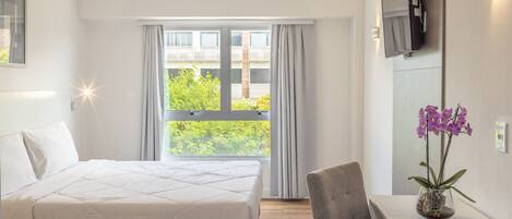 Habitación de hotel con cama, escritorio, silla, televisor montado en la pared y ventana con cortinas.