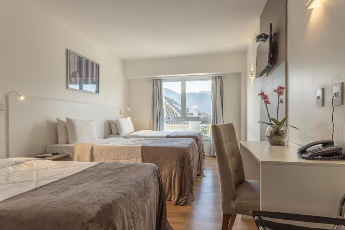 Een hotelkamer met twee bedden, een bureau en een stoel. Er is een raam met uitzicht op gebouwen en bergen.