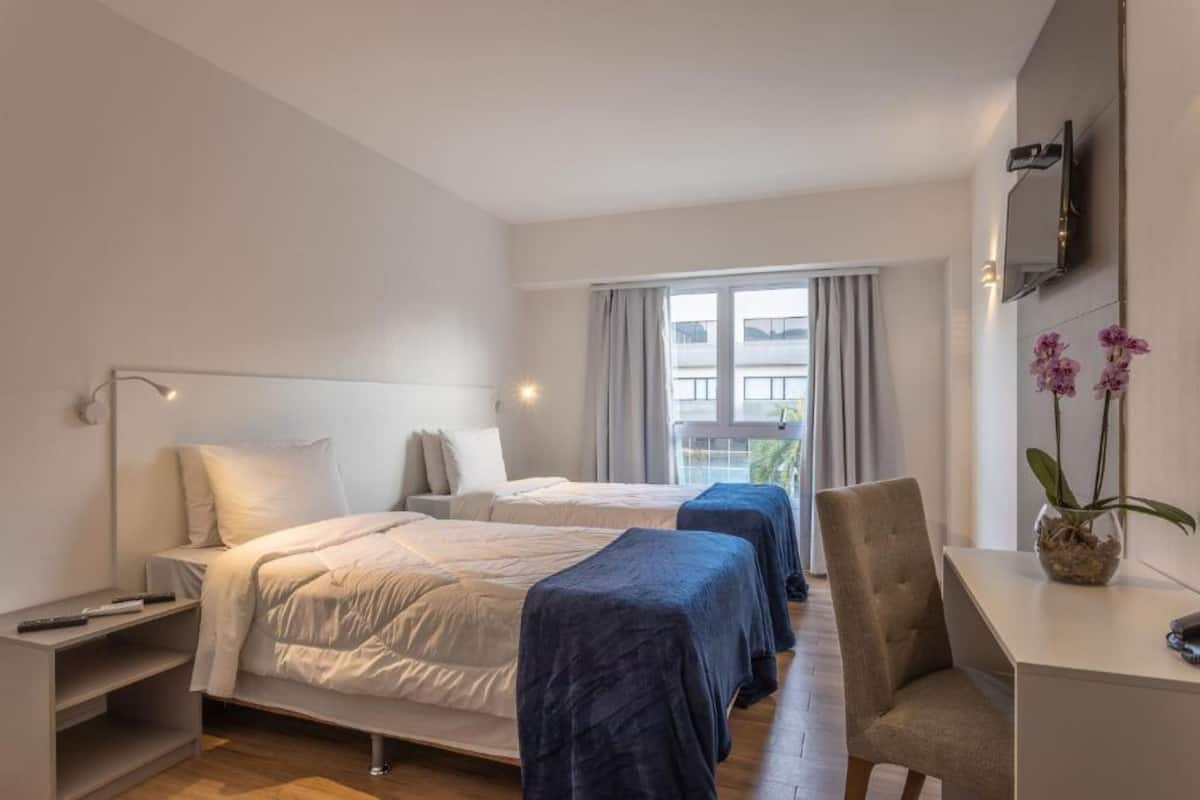 Een hotelkamer met twee bedden, een bureau, een stoel, een televisie en een raam met gordijnen.