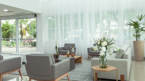 Un salon moderne avec des canapés gris, une table basse et une grande fenêtre ornée de rideaux légers.
