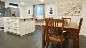 Eine moderne Küche mit weißen Schränken, einem integrierten Kühlschrank sowie einer Essecke mit Holztischen und -stühlen.