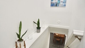 Eine Treppe mit weißen Wänden, ein kleiner Tisch mit Stühlen und zwei Zimmerpflanzen.