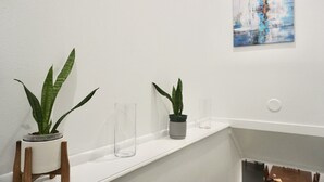 Ein modernes Badezimmer mit einem weißen Waschtisch, zwei Topfpflanzen und einer Glasvase.