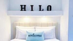 Ein Bett mit einer herzförmigen Blumenkomposition, ein Kissen mit dem Schriftzug 'welcome' und eine Wand mit den Buchstaben 'HILO'.