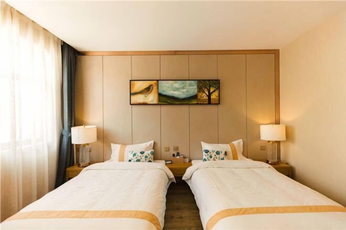 A hotel room with two beds, a painting on the wall, and a window with curtains.