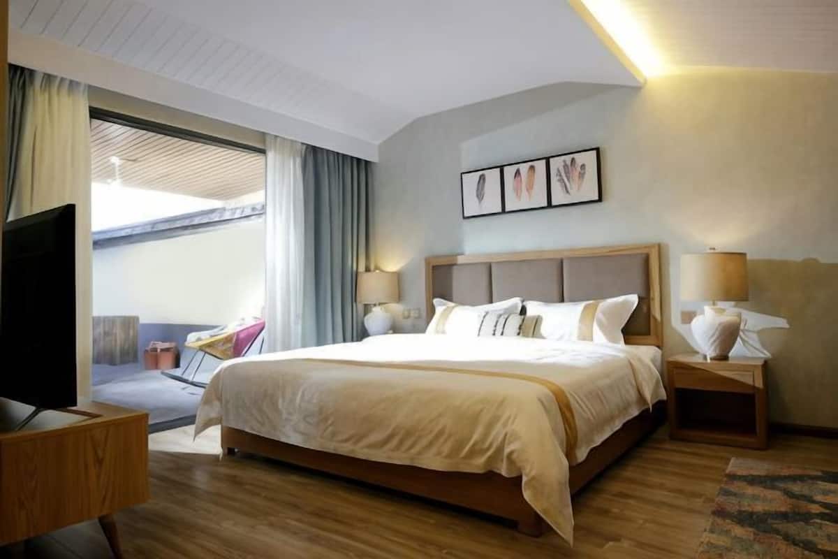 A hotel room with a large bed, bedside tables with lamps, a TV, and a balcony with a chair.