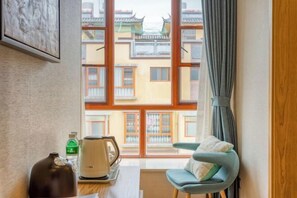 A room with a view of traditional buildings, a table with a kettle and a bottle, and a blue chair with cushions. - Pupeng Boutique Hotel (Yangbi)