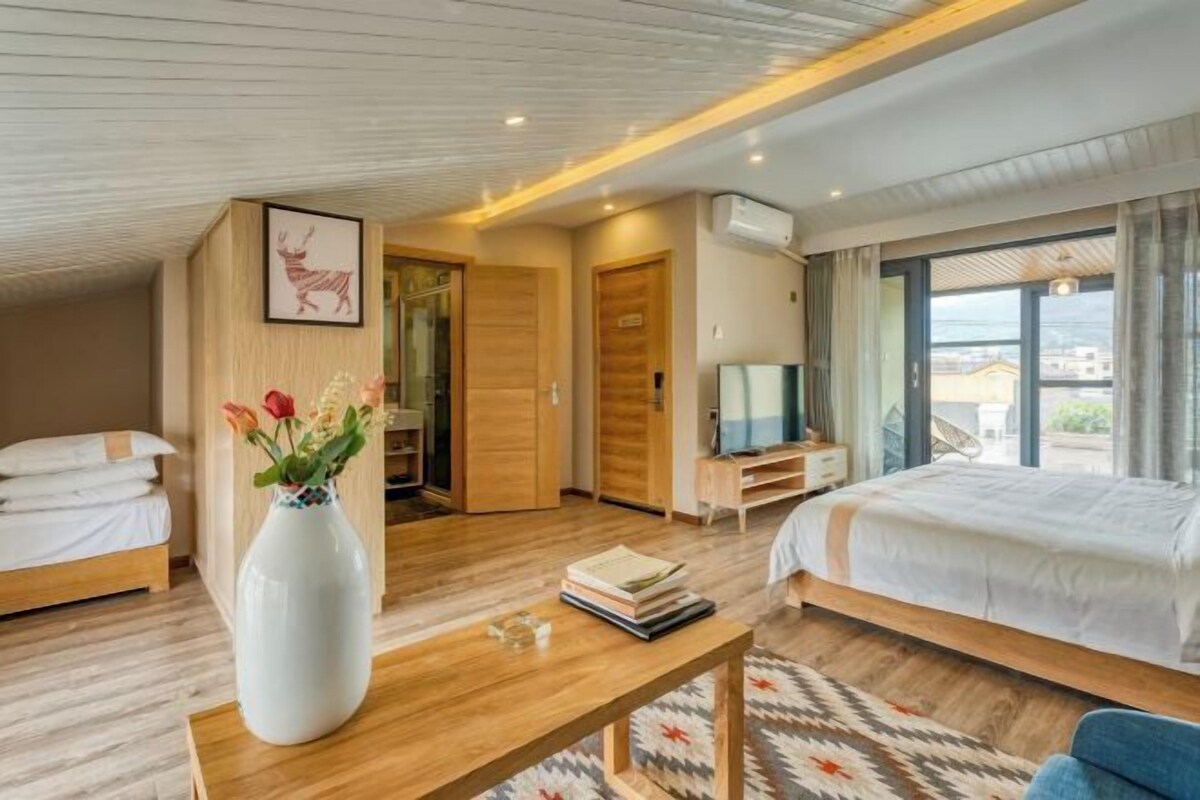 A modern hotel room with a large bed, a desk, a chair, a television, and a window with a view.