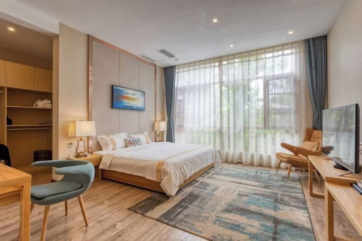 A hotel room with a bed, a desk, a chair, a TV, and a window with curtains.
