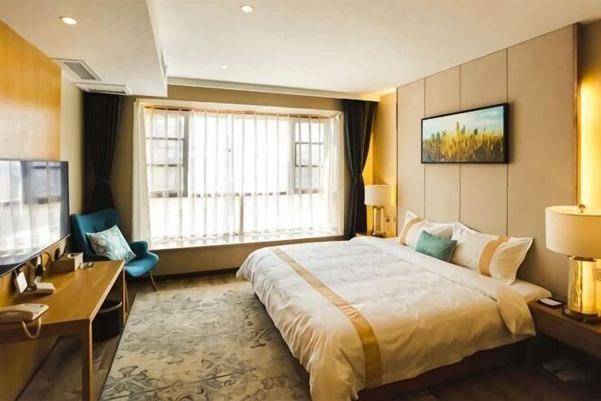 A hotel room with a large bed, a desk with a chair, a television, and a window with curtains.