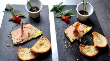 Two square black slate boards with food items and bread, each accompanied by a small white bowl with a plant.