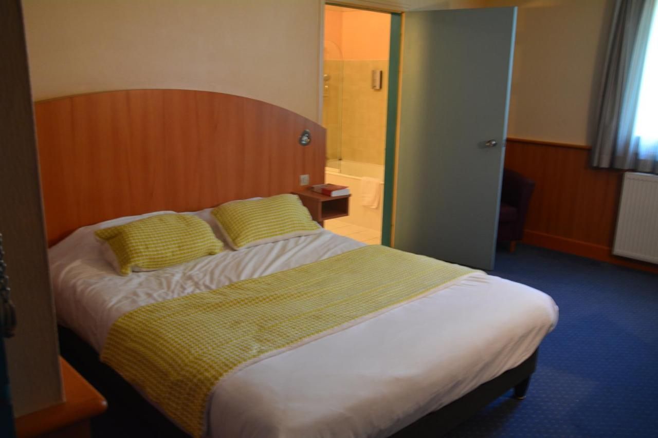 A hotel room with a bed, a bedside table, and a bathroom visible through an open door.