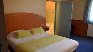 A hotel room with a bed, a bedside table, and a bathroom visible through an open door. - Logis Hotel Lucotel (Lanvollon)