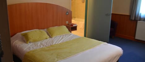 A hotel room with a bed, a bedside table, and a bathroom visible through an open door.