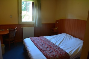 A hotel room with a bed, a desk, a chair, and a window with curtains. - Logis Hotel Lucotel (Lanvollon)