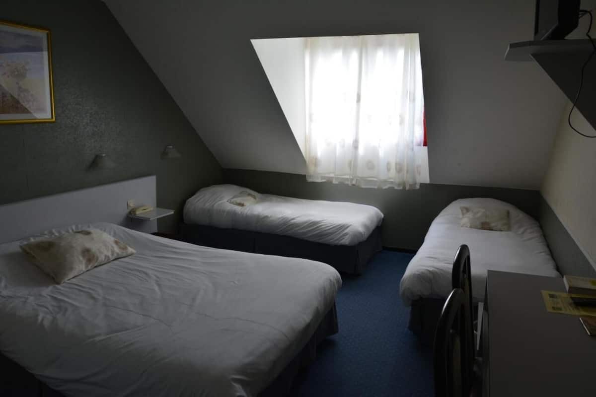 A small, dimly lit room with two single beds, a desk, and a window with sheer curtains.